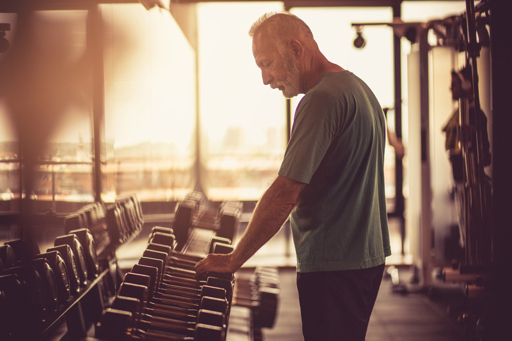 Old man in teh gym trying to pick up a dumbell.